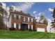 A shot of an elegant two-story brick house featuring dark shutters and a lush, green lawn under a bright sky at 10928 Jardin Way, Charlotte, NC 28215