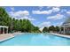 Large community pool with lounge chairs, tables, and a pergola, set against a backdrop of lush green trees and a bright blue sky at 11621 Red Knoll Ln, Pineville, NC 28134