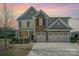 Inviting two-story home featuring a stone facade and a spacious three-car garage and manicured lawn at sunset at 276 Annatto Way, Tega Cay, SC 29708