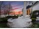 A serene backyard scene features a tranquil lake view, lush landscaping, and elegant stone patio seating at 8228 Bay Pointe Dr, Denver, NC 28037