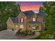 Inviting two-story brick home with a covered porch, professional landscaping, and a three-car garage at dusk at 4273 Stormy Pointe Ct, Denver, NC 28037
