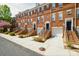 Brick townhomes with garage, stoop, and black trimmed doors in a row, with green bushes and tree in landscape at 1122 Dean Hall Ln, Matthews, NC 28105