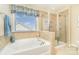 Bright bathroom features a soaking tub, glass enclosed shower, tile surround and a window with blinds at 5115 Sand Trap Ct, Monroe, NC 28112