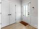 Bright foyer with light wood flooring, white trim, a front door with glass, and a mat that says 