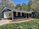 Rear view showcasing dark blue siding, brick foundation, and attached carport nestled within a serene wooded area at 923 Wyke Rd, Shelby, NC 28150
