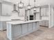 Bright kitchen features an island with pendant lighting, stainless hood, light wood floors and light gray cabinetry at 9934 Cask Way, Huntersville, NC 28078