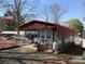 Exterior view of a single story home featuring a red metal roofed awning, propane tanks, and gravel parking area at 149 Deer Park Rd # D26/27, Mount Gilead, NC 27306