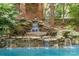 A multi-tiered stone waterfall feature flows into a swimming pool near brick house and landscaping at 2120 Malvern Rd, Charlotte, NC 28207