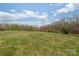 Vast open field surrounded by dense trees under a bright blue sky with scattered clouds at 3526 Harmony Hwy, Harmony, NC 28634