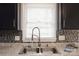 A kitchen sink is featured in front of a window, granite countertops, tile backsplash, and black cabinets at 1113 Keswick Pl # 118, Monroe, NC 28112