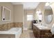 Neutral bathroom featuring a large tub with decorative tiling, a double sink vanity, and a window for natural light at 14124 Hiwassee Rd, Huntersville, NC 28078