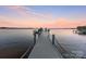Long wooden dock extending into a tranquil lake with boat slips and sunset sky at 114 Ventana Ct, Mooresville, NC 28117