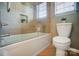 Tiled bathtub and toilet in a bathroom with glass shower door and a niche with decorative plant at 6519 Summertree Ln, Charlotte, NC 28270