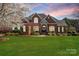 Elegant brick home with a manicured lawn and lush landscaping under a colorful sky at 3071 Ancestry Cir, Matthews, NC 28104