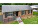 Low angle showcasing brick exterior with black shutters, a cozy covered porch, and landscaped yard at 1519 Briarfield Dr, Charlotte, NC 28205