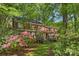 Beautiful two-story brick home surrounded by mature trees and flowering bushes, with a deck and lush lawn at 2605 Winding Oak Dr, Charlotte, NC 28270