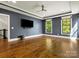 Spacious living room with hardwood floors, two large windows, a ceiling fan, and a large wall-mounted TV at 6700 Folger Dr, Charlotte, NC 28270