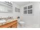 Bathroom with granite countertops, wooden cabinets, a white toilet, white walls, and a window with white shutters at 3916 Riverbend Rd, Charlotte, NC 28210