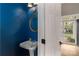 Stylish powder room with blue walls, pedestal sink, decorative mirror, and white door at 108 Kinderston Dr, Davidson, NC 28036