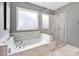 Bathroom featuring a tiled tub, a glass enclosed shower, and a frosted window that provides natural lighting at 14921 Baldridge Dr, Huntersville, NC 28078