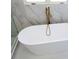 Modern bathroom featuring an elegant white tub and a gold faucet set against marble wall tiling at 3500 Manna Ln, Mount Holly, NC 28120