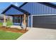 Charming blue home featuring a covered porch with stone accents and a dark gray garage door at 32525 Buchanan Ln, Albemarle, NC 28001