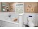 Bright bathroom with tub and window, shelving unit, toilet, white wainscoting, and neutral walls at 2792 Lakeshore Rd, Denver, NC 28037
