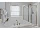 A soaking tub with bronze fixtures sits beside a glass-enclosed shower near a bright window at 8311 Camberly Rd, Huntersville, NC 28078