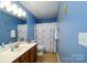 Bright bathroom with blue walls, a wood vanity, tiled floors and a shower with a stylish curtain at 8621 Sequoia Grove Ln, Charlotte, NC 28214