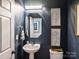 Stylish powder room with dark blue walls features a pedestal sink, decorative mirror, and elegant lighting at 516 White Tail Ter, Waxhaw, NC 28173