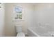 Bathroom featuring a white tub/shower combo, toilet, window view, neutral tile flooring and walls, and chrome hardware at 15814 Herring Gull Way, Charlotte, NC 28278