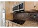 Close-up of stainless steel microwave and black cooktop above a tiled backsplash and granite countertops in a modern kitchen at 15814 Herring Gull Way, Charlotte, NC 28278
