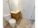 A clean bathroom with a white toilet, wood vanity, and tan tile flooring, illuminated by overhead lighting at 6525 Soapstone Dr, Charlotte, NC 28269
