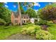 Landscaped front yard with mature trees and shrubs surround a brick home featuring black shutters and a side-entry garage at 6744 Wheeler Dr, Charlotte, NC 28211
