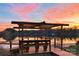 Scenic sunset view from a wooden dock overlooking a tranquil lake with covered seating at 7268 Kiskadee Dr, Denver, NC 28037