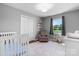 Cozy Bedroom room with a white crib, gray walls, and a comfortable reading chair by the window at 2430 Rocky Ford Rd, Newton, NC 28658