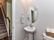 Compact powder room with pedestal sink, framed oval mirror, and convenient stairway access at 3524 Auburn Curb Rd, Charlotte, NC 28217