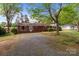 Quaint brick home with a gravel driveway and mature trees in a serene setting at 1315 Arbor Dr, Salisbury, NC 28144