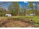 View of property with large yard, mature trees, outbuildings, and a lush green forest in the background at 612 Rowan Mill Rd, Salisbury, NC 28147