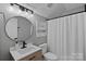 Well-lit bathroom with a wood vanity, round mirror, modern fixtures, and a shower with a white curtain at 181 Glynwater Dr, Mooresville, NC 28117