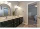 Bathroom with dual sinks, framed mirrors, black cabinets, and views into bedroom at 10643 Rippling Stream Nw Dr, Concord, NC 28027