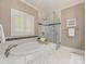 Elegant bathroom with marble tile, soaking tub, glass shower, and plantation shutters at 10626 Newberry Park Ln, Charlotte, NC 28277