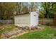 A weathered white backyard shed with a side door stands on a grassy lawn, next to a wooden fence at 1113 Urban Pl, Charlotte, NC 28209