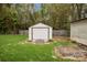 A backyard shed featuring a white facade with a garage door, sitting on a grassy lawn alongside a wooden fence at 1113 Urban Pl, Charlotte, NC 28209