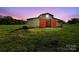 Rustic barn with red doors sits on a grassy field, featuring an open entrance under a lovely sunset backdrop at 173 Chestnut Grove Rd, Statesville, NC 28625