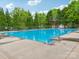 Large outdoor pool area with clear blue water, surrounded by lounge chairs and lush green trees under a sunny sky at 9612 Eagle Feathers Dr, Charlotte, NC 28214