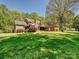 Expansive green backyard view of brick home featuring mature trees, a patio, and well-maintained landscaping at 1413 Willow Oaks Trl, Weddington, NC 28104