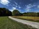 Long gravel driveway lined by a wooden fence, leading to a picturesque country home amidst lush greenery at 3014 Haigler Rd, Monroe, NC 28110