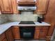 Close-up of kitchen with oven, countertop cooktop, stainless steel hood, and wood cabinets with marble backsplash at 148 Palaside Ne Dr, Concord, NC 28025