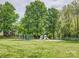 A sunny playground with swings and slides is surrounded by mature trees and a grassy field at 394 Runnymede Dr, Rock Hill, SC 29732